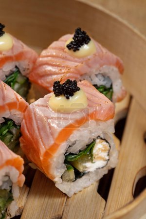Téléchargez les photos : Sushi Philadelphie au saumon, oignons verts, fromage Philadelphie et concombre. Les rouleaux reposent dans un plat léger en bois sur un fond clair. - en image libre de droit