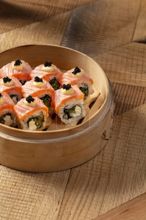 Foto de Sushi Filadelfia con salmón, cebolla verde, queso Filadelfia y pepino. Los rollos se encuentran en un plato ligero de madera sobre un fondo claro. - Imagen libre de derechos