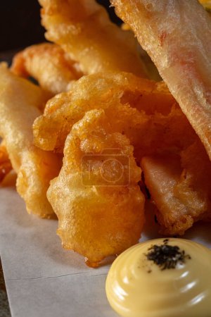 Photo for Paprika, onions, carrots and shrimp fried in batter in deep fat on light paper lie on a ceramic plate. - Royalty Free Image
