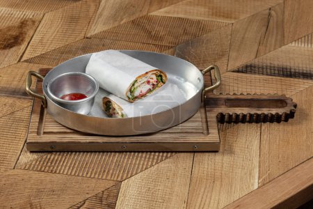 Photo for Shawarma with crab meat, lettuce, cabbage and chopped chili peppers in thin pita bread wrapped in light paper. Nearby is a bowl of sweet and sour chili sauce. The food is in a metal bowl. - Royalty Free Image