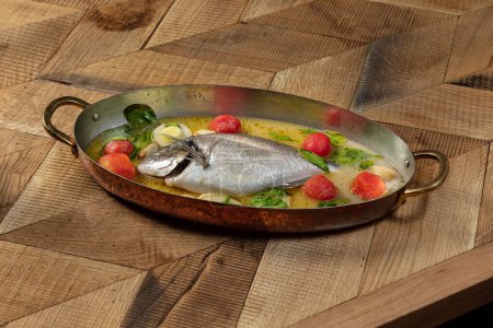 Photo for Whole dorado fish baked in white wine with leek, cilantro and cherry tomatoes in a creamy garlic sauce and white wine. Food is in a metal bowl - Royalty Free Image