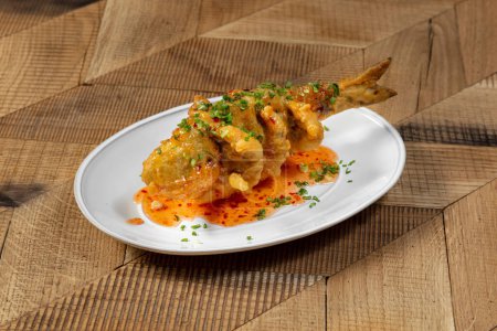 Photo for Sea bass baked whole breaded with sweet and sour sauce on a light plate. Garnished with finely chopped green onions and sweet and sour sauce. - Royalty Free Image
