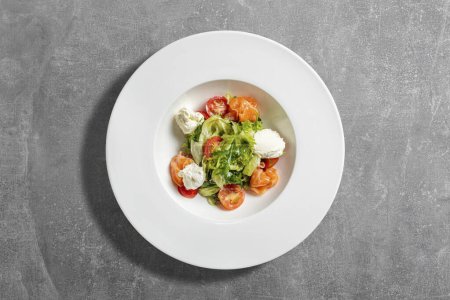 Photo for Summer salad with arugula, mozzarella, cherry tomatoes, salmon in pesto sauce. Food lies in a light ceramic plate on a gray stone background. - Royalty Free Image