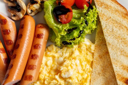 Photo for Scrambled eggs with sausages and toast, lettuce, cherry tomatoes and mushrooms in balsamic sauce. Food lies on a light ceramic plate on a gray stone background. - Royalty Free Image