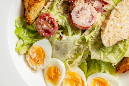 Photo for Caesar salad with chicken, cherry tomatoes, croutons, quail eggs, lettuce and garlic sauce in a light ceramic plate. The plate stands on a gray stone background. - Royalty Free Image