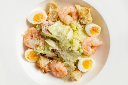 Photo for Caesar salad with shrimp, cherry tomatoes, croutons, quail eggs, lettuce and garlic sauce in a light ceramic plate. The plate stands on a gray stone background. - Royalty Free Image