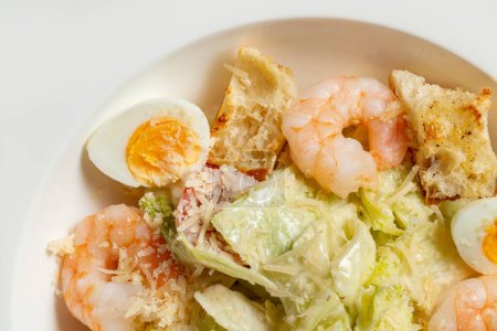 Photo for Caesar salad with shrimp, cherry tomatoes, croutons, quail eggs, lettuce and garlic sauce in a light ceramic plate. The plate stands on a gray stone background. - Royalty Free Image