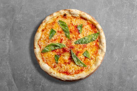Foto de Pizza Margherita de masa fermentada con salsa de tomate, queso mozzarella y hojas de albahaca. Pizza se encuentra sobre un fondo de piedra gris. - Imagen libre de derechos