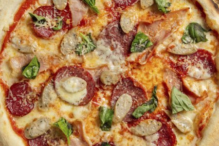 Téléchargez les photos : Pizza au levain avec viande et saucisses, myr mozzarella, sauce tomate et feuilles de basilic. Pizza repose sur un fond de pierre grise. - en image libre de droit