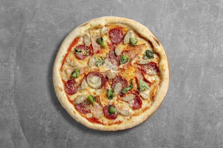 Foto de Pizza con masa fermentada con carne y embutidos, mozzarella myr, salsa de tomate y hojas de albahaca. Pizza se encuentra sobre un fondo de piedra gris. - Imagen libre de derechos