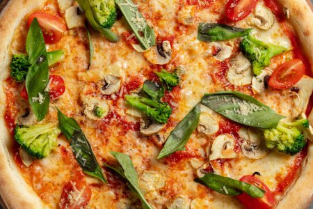 Foto de Pizza vegetariana de masa fermentada con verduras, champiñones, hojas de albahaca, queso parmesano y salsa de tomate; La pizza se encuentra sobre un fondo de piedra gris. - Imagen libre de derechos