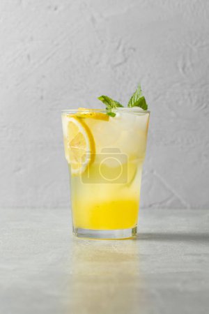 Foto de Un vaso de limonada casera con limón, lima y naranja, cubitos de hielo y hojas de menta en una taza de vidrio transparente sobre un fondo de piedra gris. - Imagen libre de derechos