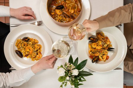 Photo for Homemade pasta with shrimp, salmon, mussels in a wine-cream sauce in a copper dish with a handle and baked in the oven under a dough lid. Place the dishes on a table with a light tablecloth. The waiter uses a fork and a spoon to place pasta and white - Royalty Free Image