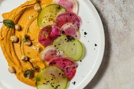 Photo for Hummus pasta with pumpkin and hazelnuts, radish slices of different colors and microgreen sprouts. Food lies in a light ceramic plate on a colored background. - Royalty Free Image