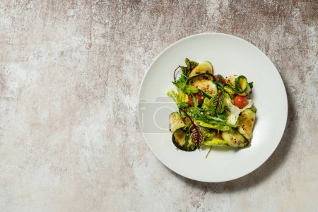 Photo for Vegetable mix salad with zucchini, cherry tomatoes, pine nuts, olive oil and balsamic sauce. Food lies in a light ceramic plate on a colored background. - Royalty Free Image