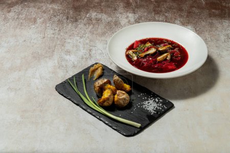 Photo for Ukrainian fasting soup borscht, with mushrooms and vegetables in a light ceramic plate. Nearby is a slate plate with fried potatoes and green onions. Dishes stand on a light fabric background. - Royalty Free Image