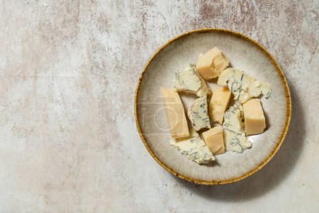 Photo for Ukrainian parmesan and dorblyu cheese cut into pieces and lying in a ceramic plate on a light fabric background. - Royalty Free Image