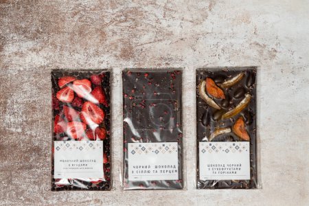 Téléchargez les photos : Trois types de chocolat avec fruits, noix, poivre et fraise dans l'emballage et les étiquettes reposent sur un fond de tissu léger. - en image libre de droit