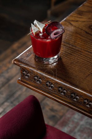 Foto de Un cóctel Bloody Mary con jugo de remolacha, trozos de queso de cabra y chips de remolacha se encuentra en una encimera de madera oscura en la esquina de la mesa. - Imagen libre de derechos