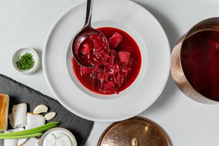 Foto de Sopa de borscht ucraniano en un plato de cerámica redondo y ligero. Cerca se encuentra un soporte de pizarra con rosquillas de ajo y trozos de manteca de cerdo. - Imagen libre de derechos