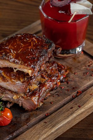 Photo for Ribbon of pork ribs in spicy chili sauce with cherry tomatoes and microgreen sprouts on a wooden board. The board stands on a light fabric background. - Royalty Free Image