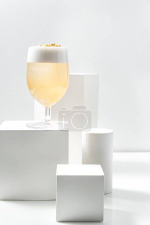 Photo for Cocktail Penicillin with citrus foam and gold leaf in a stemmed glass stands on a plaster figure among other plaster figures. All items are on a white background. - Royalty Free Image