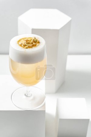 Photo for Cocktail Penicillin with citrus foam and gold leaf in a stemmed glass stands on a plaster figure among other plaster figures. All items are on a white background. - Royalty Free Image