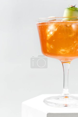 Photo for Aperol Spritz cocktail with ice cubes and a slice of cucumber in a transparent stemmed glass. The cocktail stands on a plaster figure among other plaster figures on a white background. - Royalty Free Image