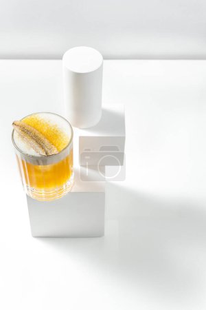 Photo for Mango Sour cocktail in a transparent glass with a piece of ice and citrus foam, topped with banana and mango powder. The cocktail stands on a plaster figure among other figures on a white background. - Royalty Free Image