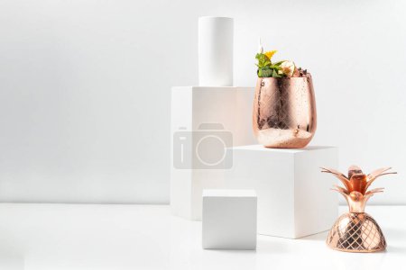 Photo for Tiki cocktail on several types of rum with fruits, berries and small ice in a copper glass on a copper stand. The cocktail stands on a plaster figure among plaster figures on a white background. - Royalty Free Image