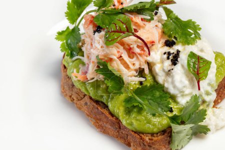 Photo for Bruschetta with poached egg, avocado puree, lettuce and parsley with crabmeat on top. Food on a light ceramic plate, on a table with a light tablecloth. Nearby is a vase and cutlery. - Royalty Free Image