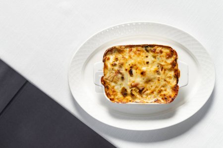 Foto de Lasaña vegetal casera en un plato de cerámica con queso parmesano rallado en la parte superior. El plato está sobre una mesa con un mantel ligero. - Imagen libre de derechos
