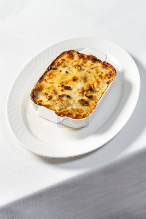Téléchargez les photos : Lasagnes maison aux légumes dans un plat en céramique avec du parmesan râpé sur le dessus. Le plat est sur une table avec une nappe légère. - en image libre de droit