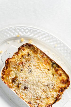 Foto de Lasaña vegetal casera en un plato de cerámica con queso parmesano rallado en la parte superior. El plato está sobre una mesa con un mantel ligero. - Imagen libre de derechos