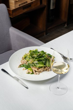 Photo for Mix salad with chicken breast and Parmesan cheese on a light ceramic plate. The plate is on a light tablecloth, next to it is a glass of white wine and cutlery. - Royalty Free Image