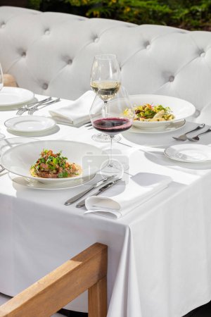 Téléchargez les photos : Steak aux champignons chanterelle et salade à la truite dans des assiettes en céramique légère sur une nappe légère. Il y a des verres de vin rouge et blanc à proximité. - en image libre de droit