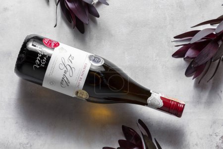 Photo for A bottle of Spier Pinotage 21 Gables rests on a light-colored linen cloth, with purple plant petals visible around the edges of the photo. Top view. - Royalty Free Image