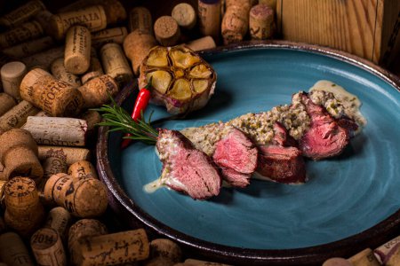 Téléchargez les photos : Steak de porc frit, sauce, romarin, ail et poivre dans une assiette posée sur un ensemble de bouchons de vin - en image libre de droit