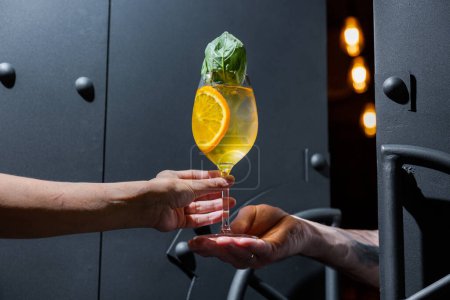 Téléchargez les photos : Cocktail with orange ice and basil in hand on the background of black doors - en image libre de droit