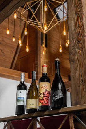 Foto de Diferentes botellas de vino, rojo, blanco y brillante soporte en un soporte de metal contra una pared de luz y vigas de madera. - Imagen libre de derechos