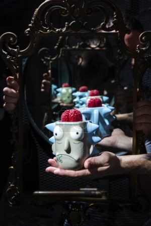 Téléchargez les photos : Cocktail avec cervelle de confiture dans un verre en forme de tête tenue par une main sur le fond d'un miroir - en image libre de droit
