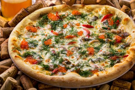 Téléchargez les photos : Pizza au fromage, caviar de saumon, coq, bacon et tomates sur une assiette posée sur un ensemble de bouchons de vin avec supports à vin - en image libre de droit