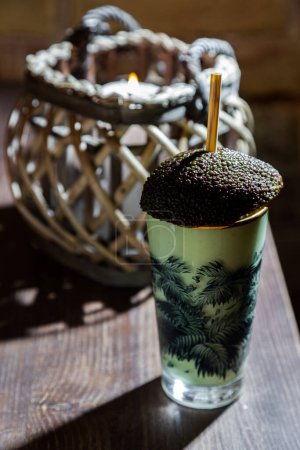 Photo for A cocktail with an avocado and a straw that stands on the table against the background of a burning candle - Royalty Free Image