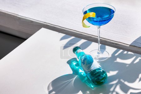 Téléchargez les photos : Cocktail bleu avec écorce d'orange dans un verre qui se tient sur la table avec une bouteille de boisson - en image libre de droit