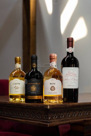 Foto de Botellas de diferentes tipos de vino Masca del Tacco en una mesa oscura cerca de una pared de luz. - Imagen libre de derechos