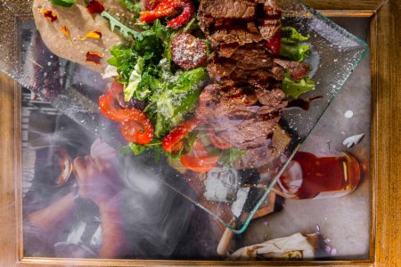 Foto de Ensalada con carne frita, pimientos, rúcula, ensalada de frisse, tomates, parmesano y salsa en un plato sobre la mesa sobre el fondo de un marco fotográfico - Imagen libre de derechos