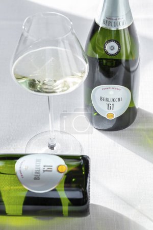 Téléchargez les photos : Une bouteille de vin mousseux Berlucchi 61 se dresse sur un fond clair. A proximité se trouve un verre avec du vin mousseux versé dedans et une autre bouteille se trouve. - en image libre de droit