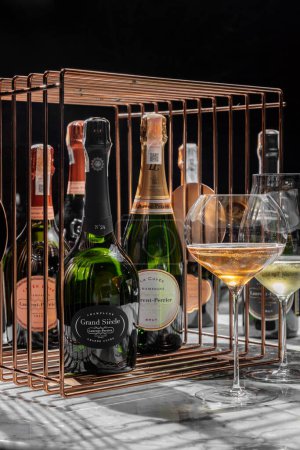 Foto de Numerosas botellas de vino espumoso Laurent-Perrier están en una jaula de bronce. Cerca están las copas con vino espumoso blanco y rosa. - Imagen libre de derechos