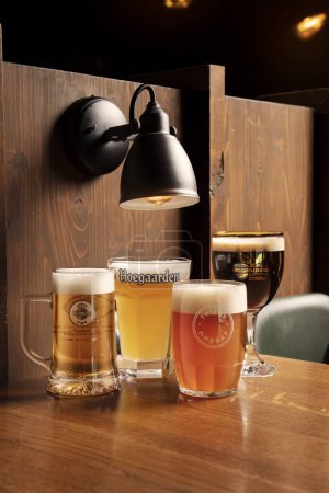 Foto de Cuatro tipos de cerveza en vasos se coloca en la mesa con bombillas brillantes en el fondo - Imagen libre de derechos