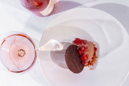 Foto de Chocolate ice cream with cranberries. A scoop of chocolate ice cream, on a bed of corn flakes and topped with cranberries in liqueur. Nearby is a large chocolate medal. Ice cream lies in a light, round, ceramic plate with wide sides. The plate stands - Imagen libre de derechos
